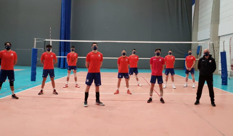 nueve jugadores con short, polera y zapatillas y un entrenador con buzo y zapatillas en cancha de voleibol, formados, con distancia social
